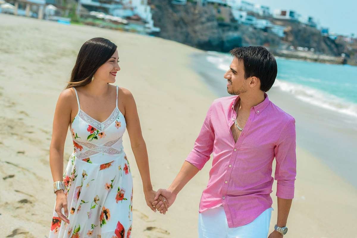Pareja de la mano paseando por la arena, mirándose