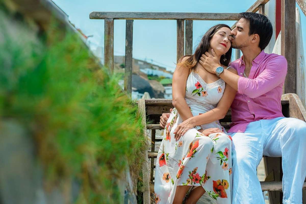 Pareja sentada en unas escaleras de madera junto a la playa