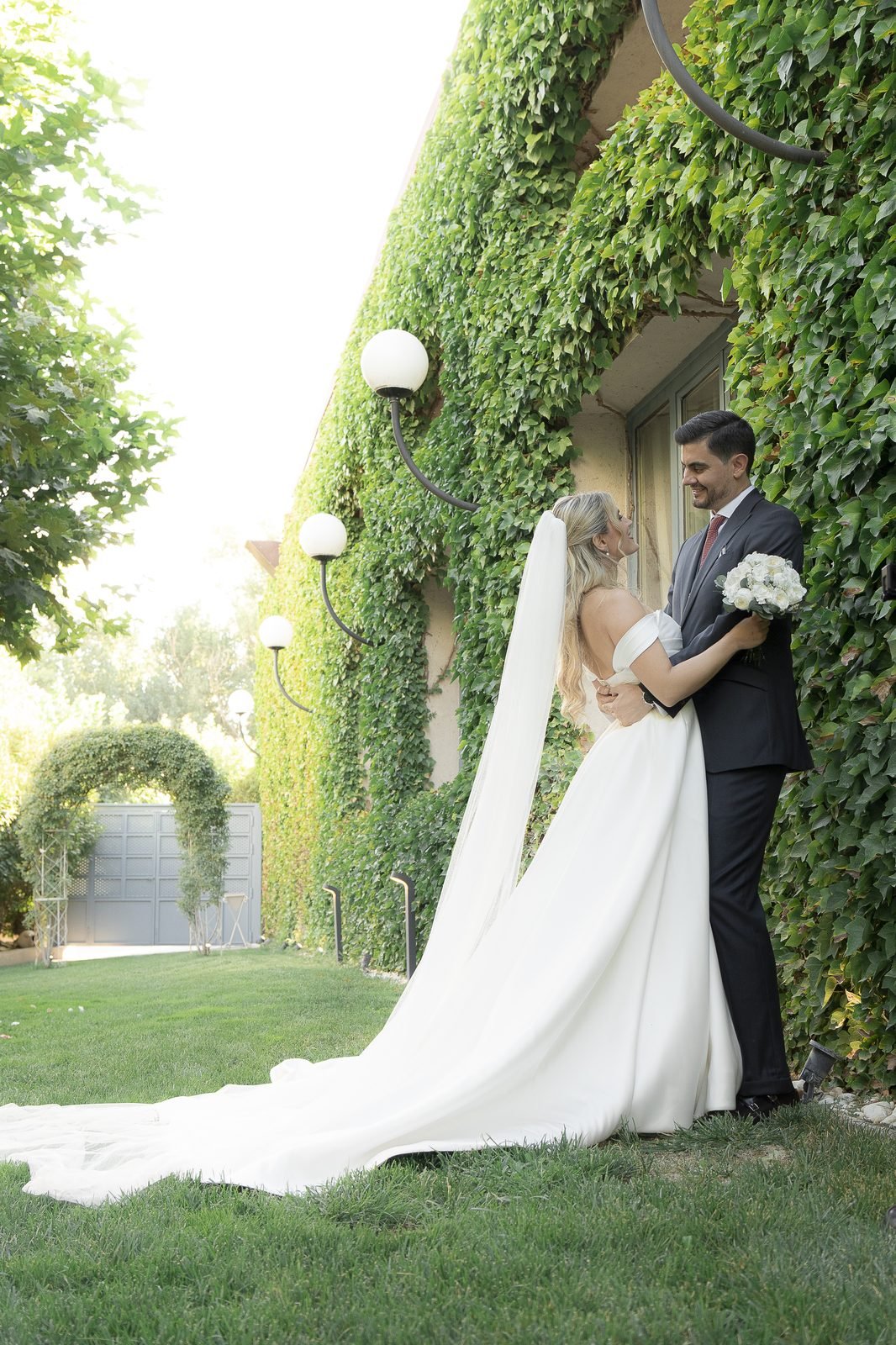 La novia con la cola del vestido extendida junto al muro de hiedra del jardín de Finca Monteviejo