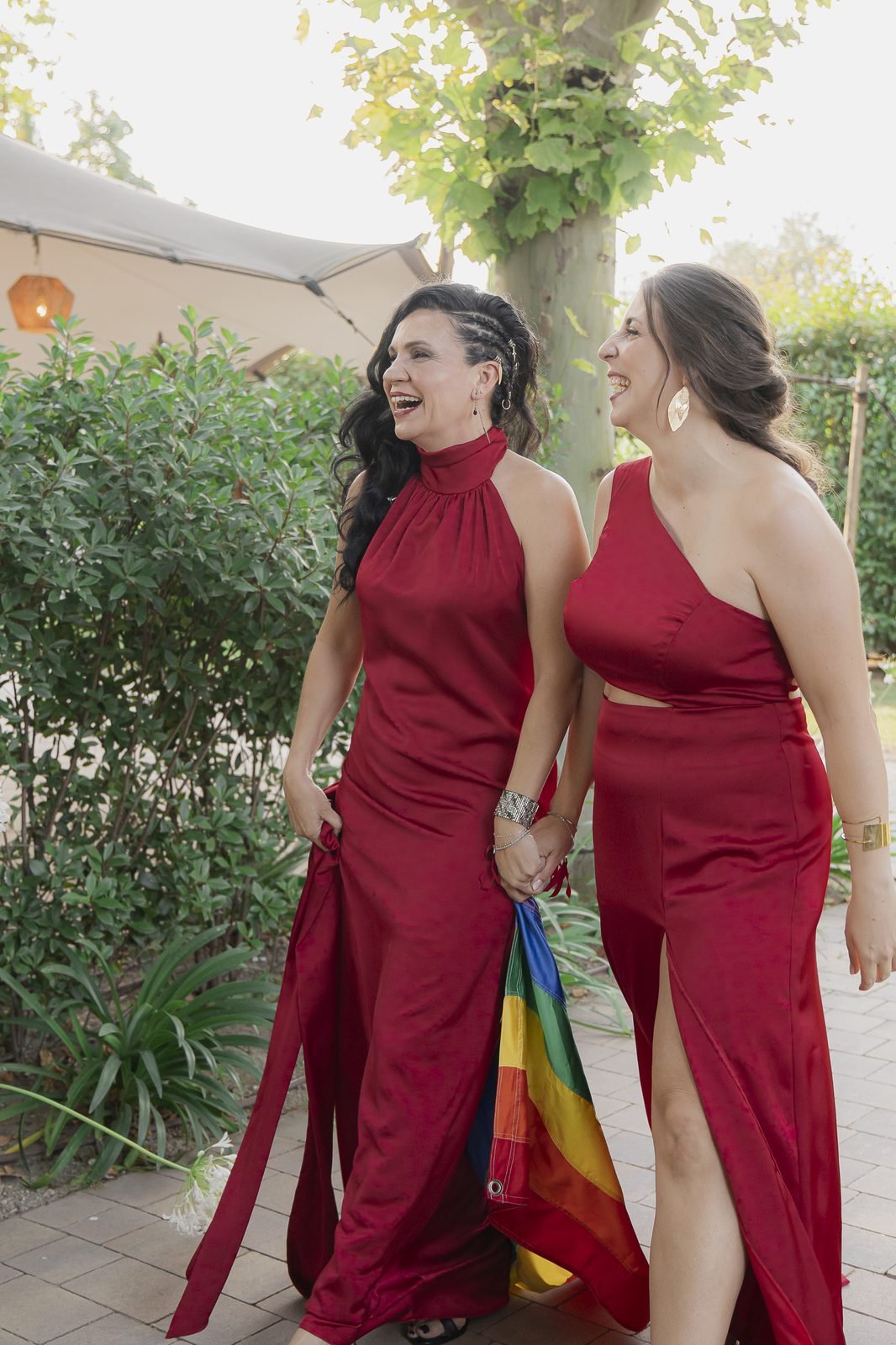 Las dos novias caminan de la mano por el jardín de Finca Solimpar con una bandera arcoíris