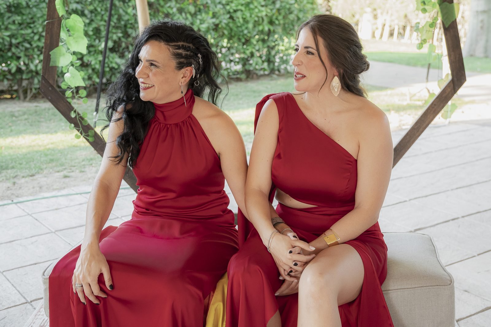Las dos novias sentadas juntas, riéndose, con el jardín detrás